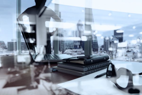 double exposure of business documents on office table with smart phone and digital tablet and london city blurred view and man thinking in the background